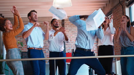 business team celebrating in multi-cultural office with colleagues throwing paperwork in the air