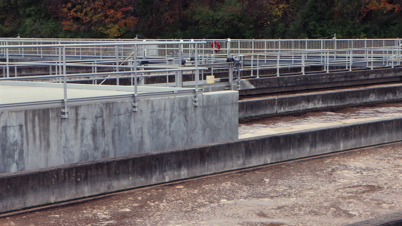 Foaming brown wastewater surges through aeration basins at a wastewater treatment plant, captured in a smooth right-to-left pan, revealing turbulent industrial flow
