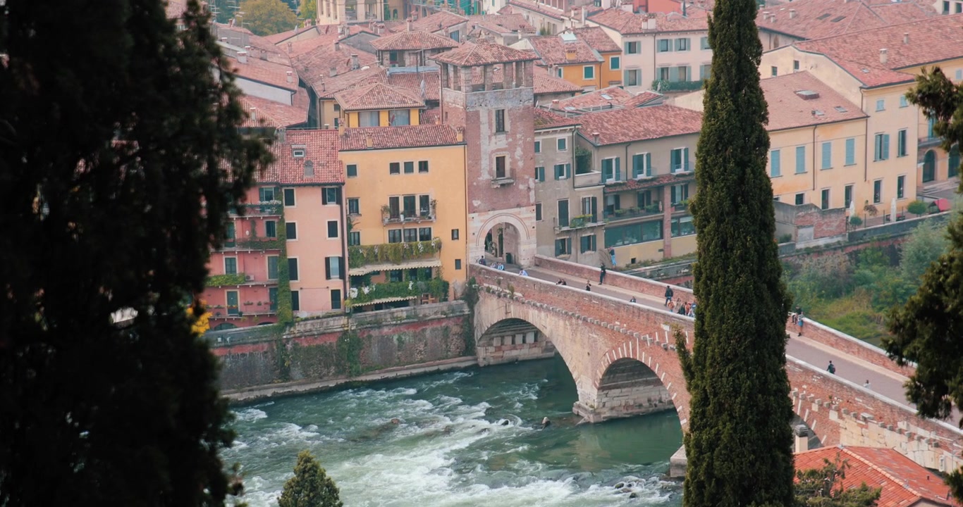 Slow motion clip of the Landscape of Verona, Italy, with a particular focus on the Ponte Pietra Bridge. Tourists and pedestrians are walking on it.