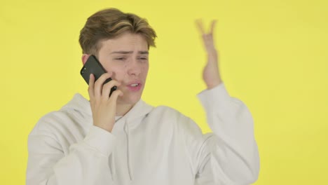 joven hablando enojado por teléfono en fondo amarillo