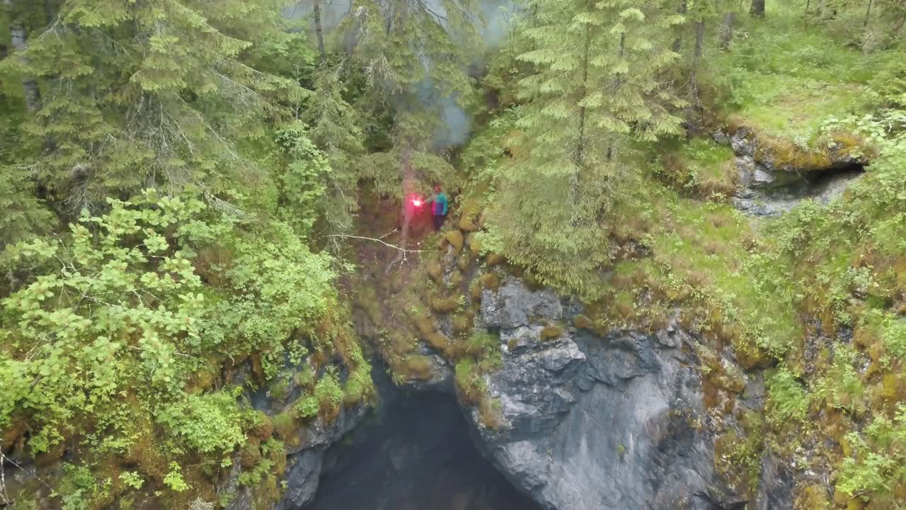 vista aérea de una persona con una llamarada roja cerca de una cueva en un bosque