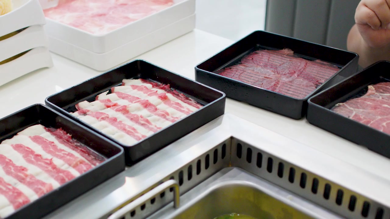 A person arranges several trays of thinly sliced raw beef on a white restaurant table