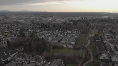wide aerial view flying over suburban neighbourhood filled with town homes grassy areas and a footpath