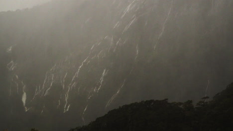 numerous waterfalls flow down a cliff face shrouded by clouds during heave rain