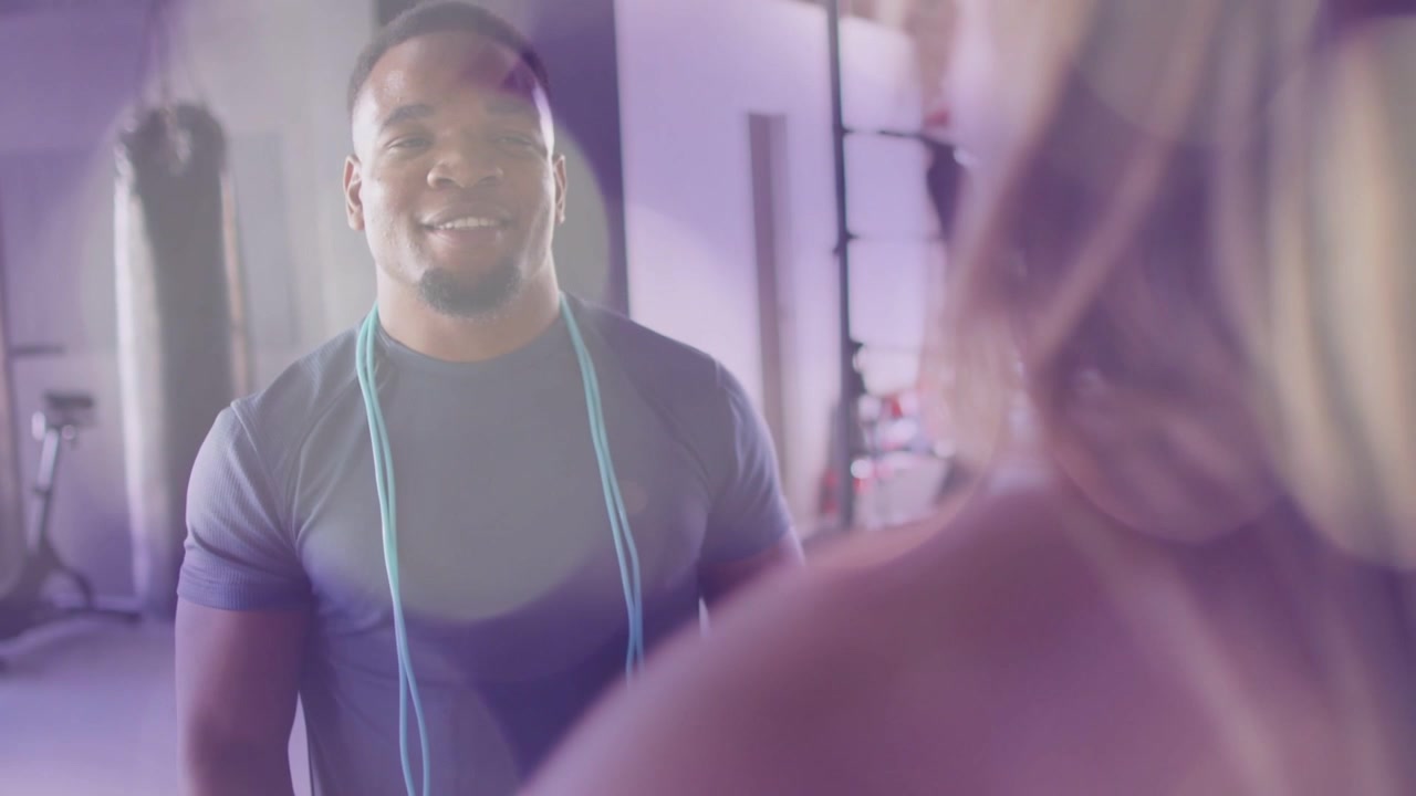 Fitness trainer pointing to client, guiding jump rope amid purple lens flares highlighting motion