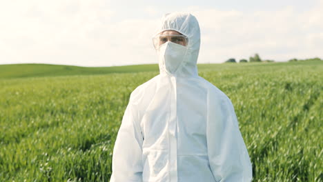 caucasian researcher man in white protective suit and goggles doing pest control in the green field