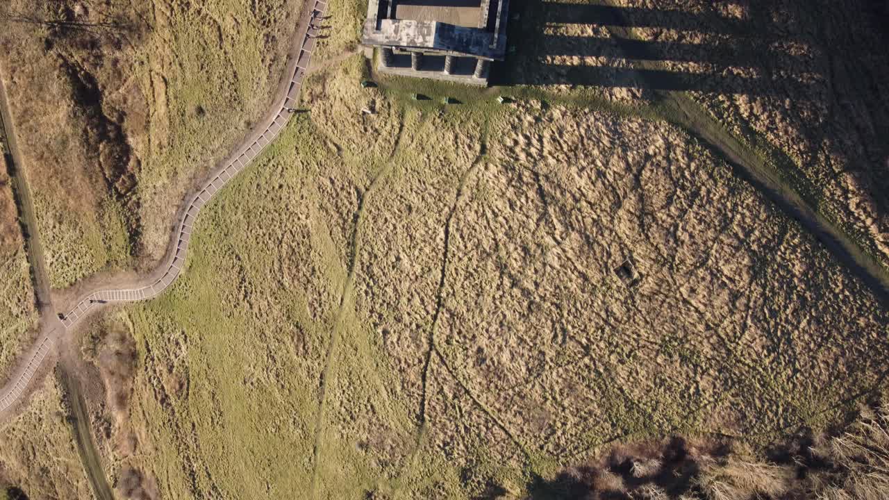 vista aérea de pájaro sobre una antigua estructura histórica de pilares con turistas que ascienden hasta la cima de la colina al atardecer