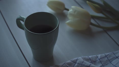 tea cup on wooden table with tulips and a sheet resting on it