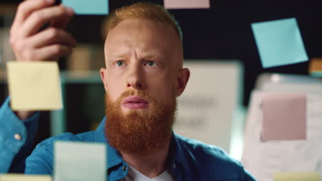 Focused hipster guy posting stickers at working board in modern workplace.