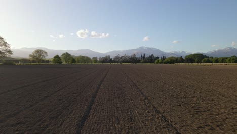 low, fast drone flight over freshly ploughed farm land during sunset, mountain range in background