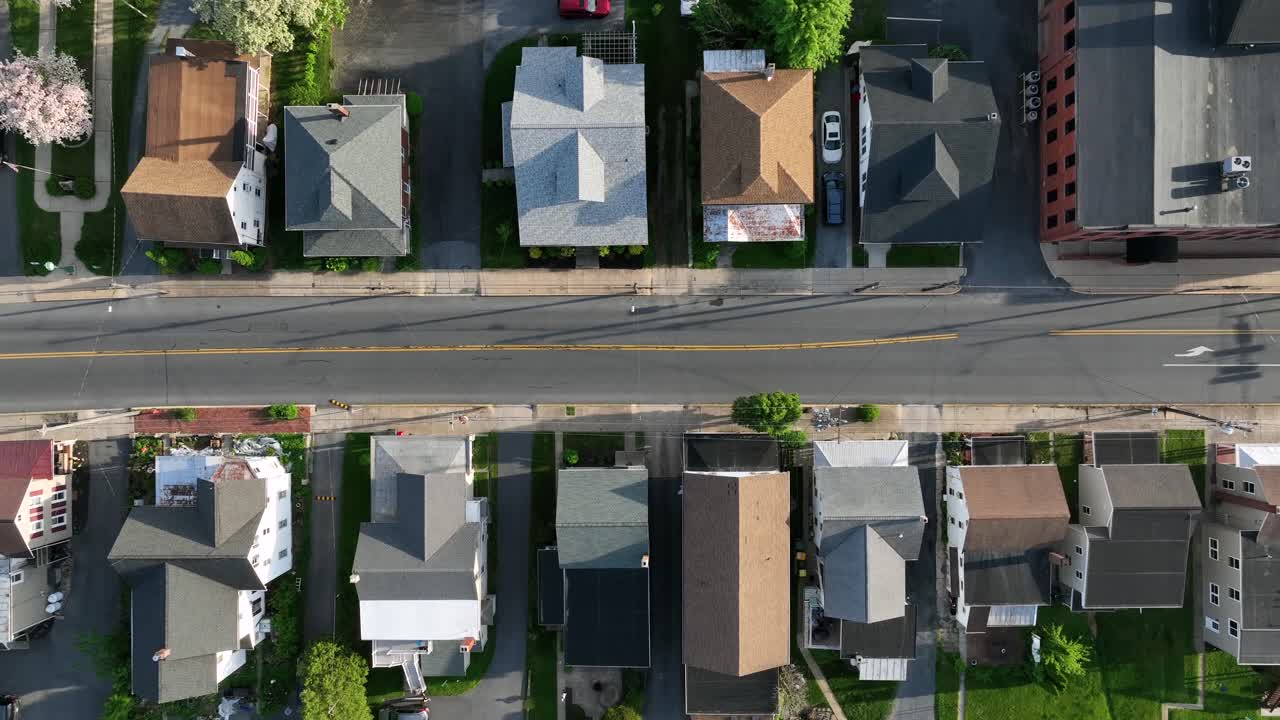 Small row of homes along straight street with blossoming trees in springtime. Aerial top down rising shot. Rooftops of houses in american town.