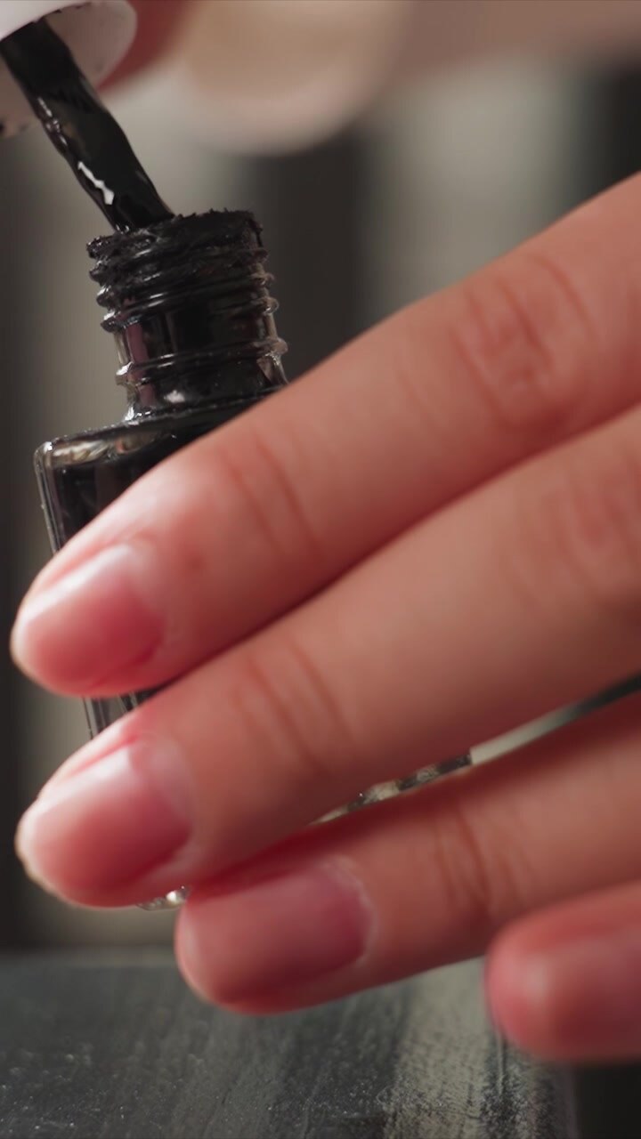 Close up sequence shows woman hands as woman unscrews cap from bottle of black nail polish. focus remains tightly on her fingers and glossy texture of liquid capturing details