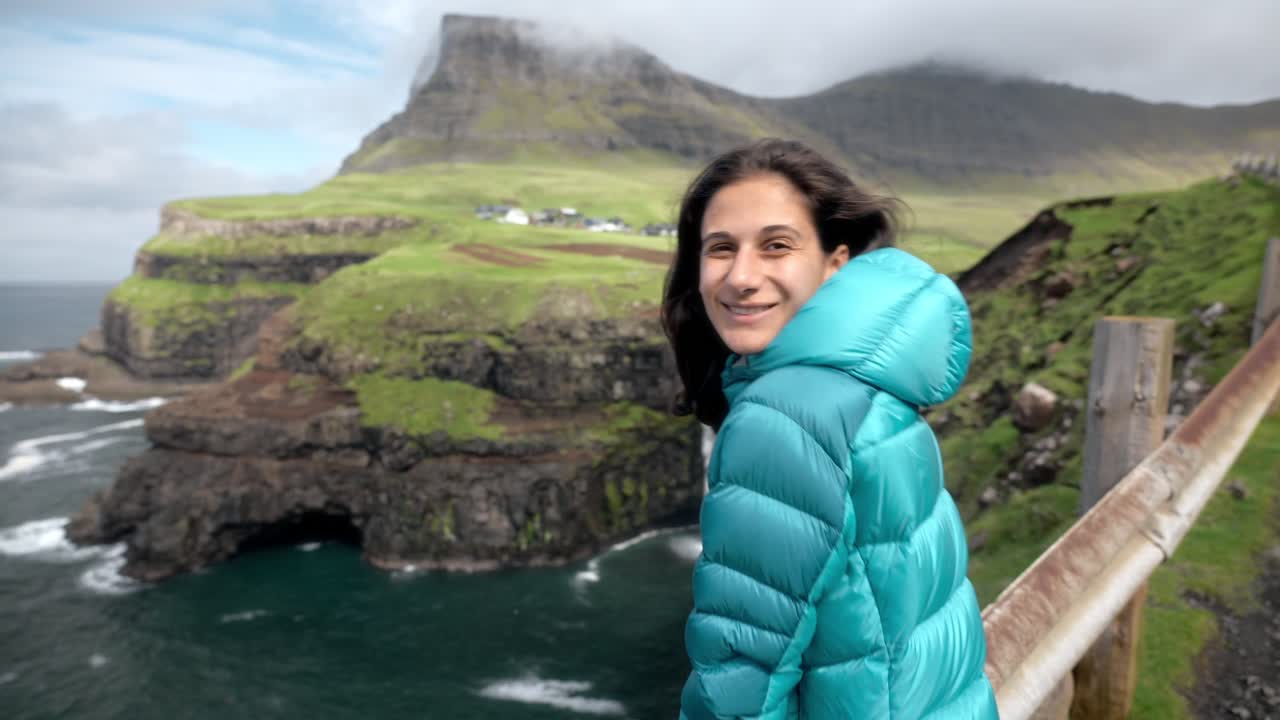 A woman stands by a scenic viewpoint in Gásadalur, Faroe Islands, near a waterfall