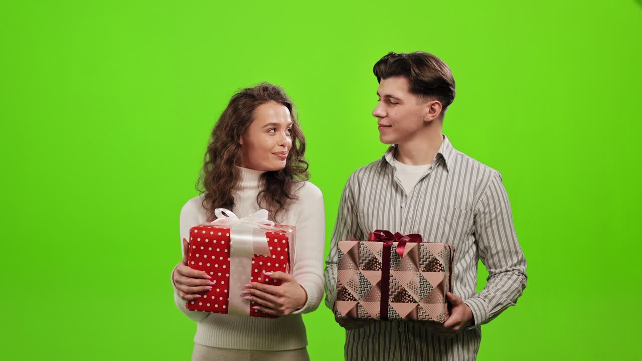 한 남녀가 선물을 들고 웃으며 서로를 바라보며 녹색 바탕에 서 있다.