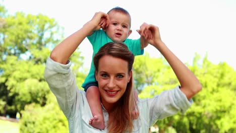 madre feliz sosteniendo a un bebé lindo en sus hombros en el parque