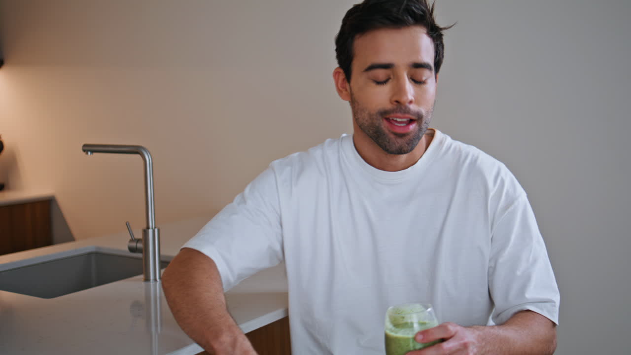 Man tasting green smoothie at home kitchen enjoying healthy nutrition closeup