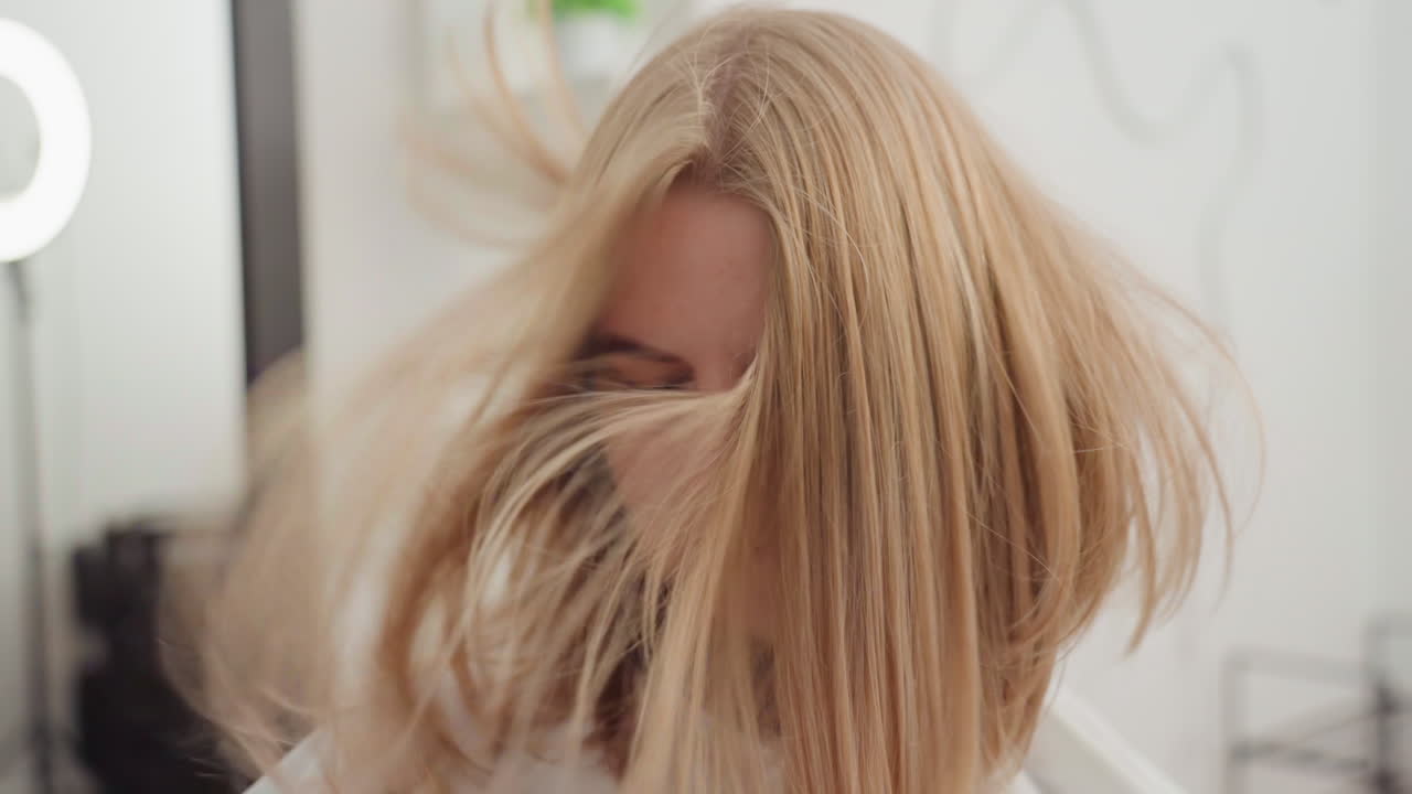 Donna bionda platino che muove i capelli con energia in un salone: la sequenza mostra movimenti ampi e dettagli increspati, primi piani in movimento con illuminazione da studio, pose da modello editoriale combinate con un tocco giocoso