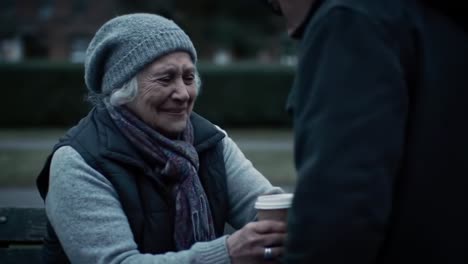 in a peaceful park setting, an elderly woman wearing a cozy hat and scarf shares a heartfelt moment with a man.