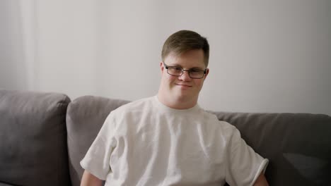 retrato de un hombre caucásico feliz en camiseta blanca con síndrome de down sentado en el sofá en casa