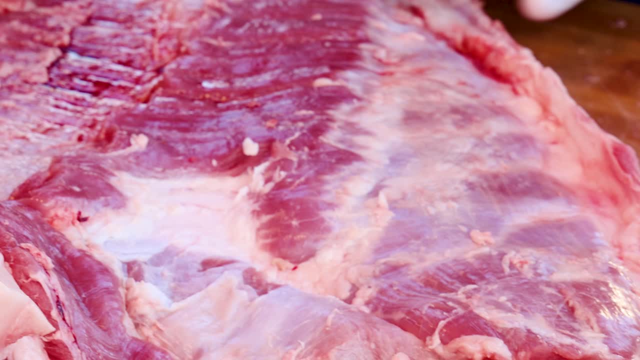 La telecamera effettua una lenta panoramica su carne di manzo cruda marmorizzata, evidenziando la consistenza del grasso sotto la luce intensa del mercato