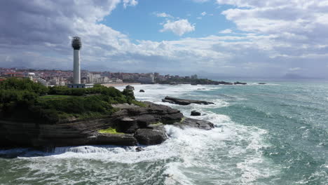 big waves crashing on biarritz lighthouse sunny day aerial view