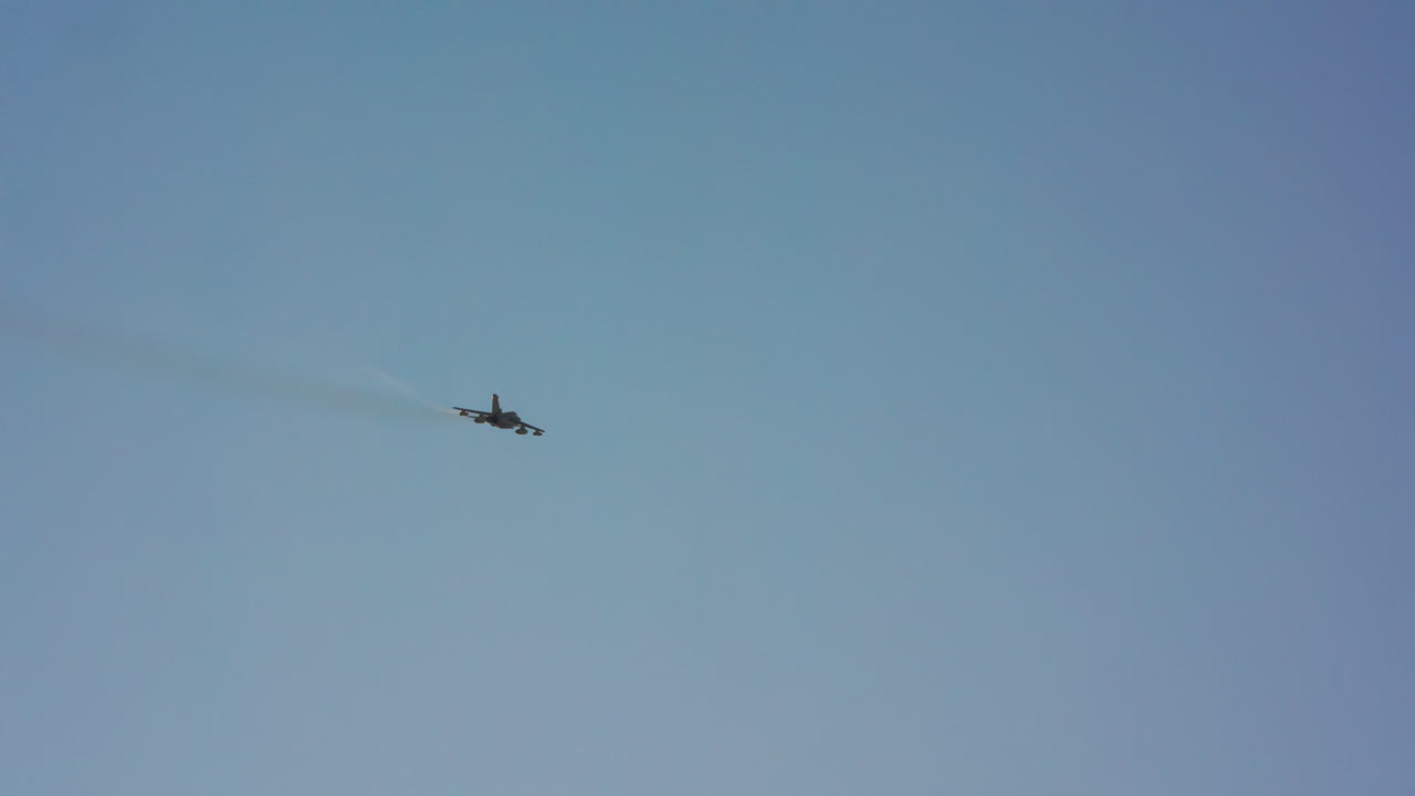 Military Jet Flying Across a Clear Blue Sky with Contrail