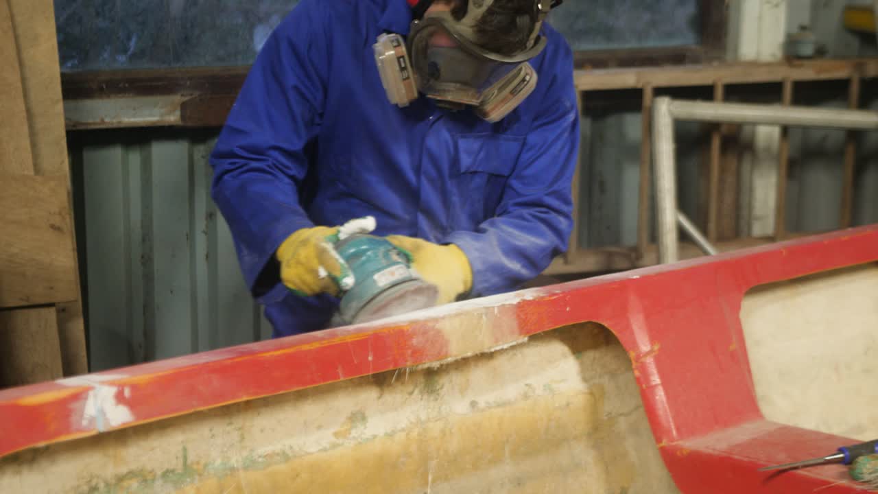 Sanding repaired gunwale of fiberglass fishing boat using orbital sander