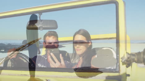 taking selfie in yellow convertible, couple with surfboard silhouette in background