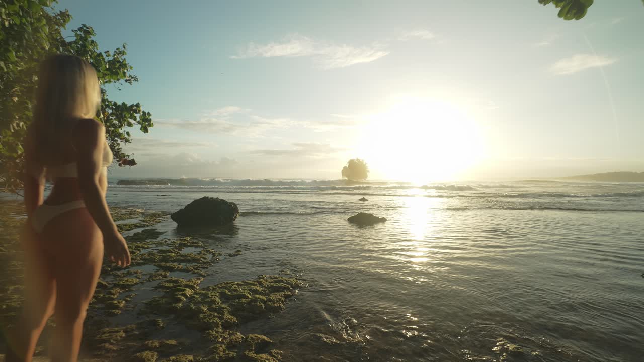 mujer en forma en bikini blanco empapándose en la brillante luz del sol de la mañana por encima del horizonte