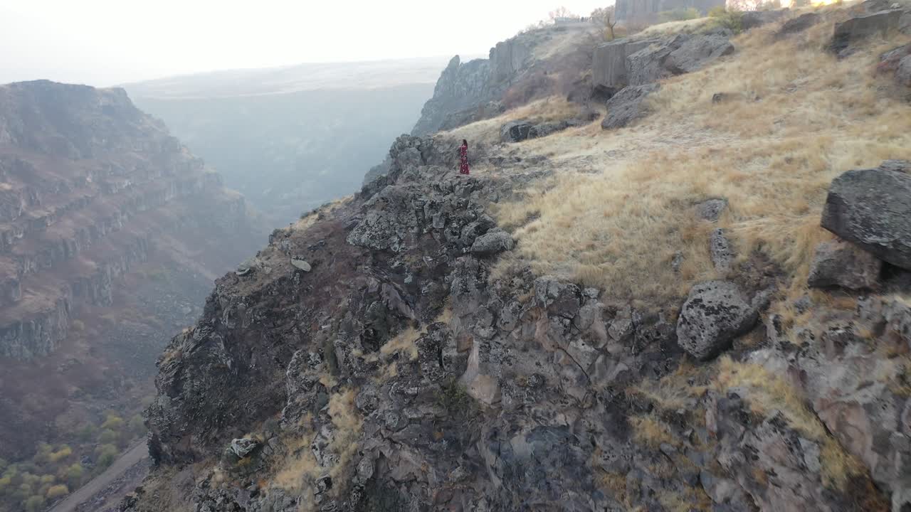 Terreno roccioso e scosceso a strapiombo che scende in un'ampia valle con pareti rocciose stratificate e formazioni terrestri distanti che sfumano nella foschia atmosferica.