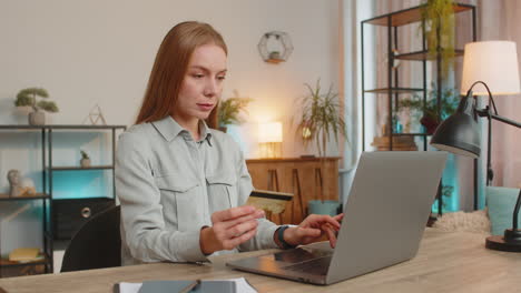 happy caucasian woman freelancer using credit card and laptop for online shopping at table at home