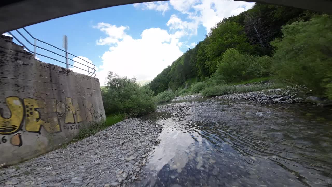 Aerial image of a drone flying upstream over a river, passing over a dam, and crossing under a bridge