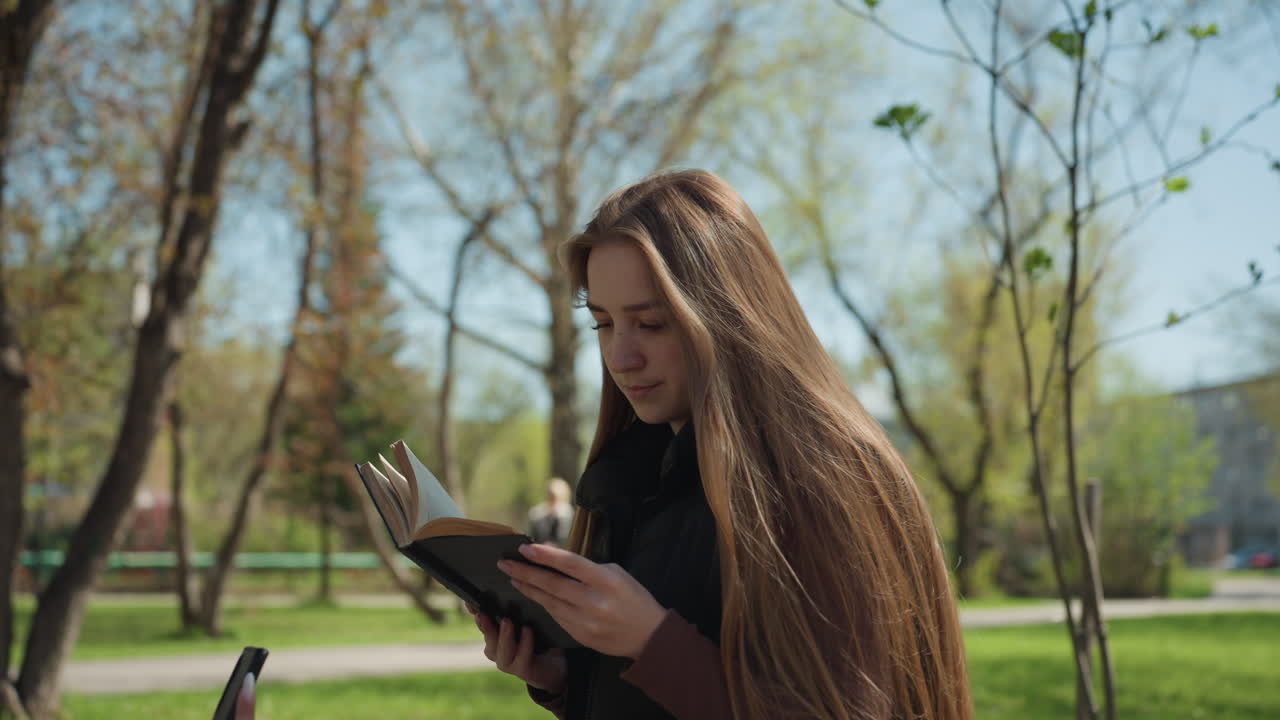 Estudiante repasando al aire libre, joven de ascendencia europea revisando apuntes bajo el follaje iluminado por el sol, ambiente informal en el campus con una joven concentrada preparándose para los exámenes bajo árboles soleados