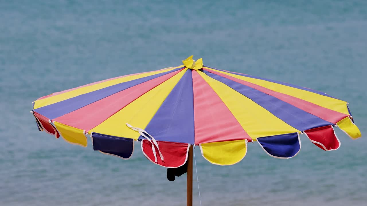 A vibrant beach umbrella sways gently in the wind against a serene ocean backdrop, capturing the essence of a breezy day in Phuket