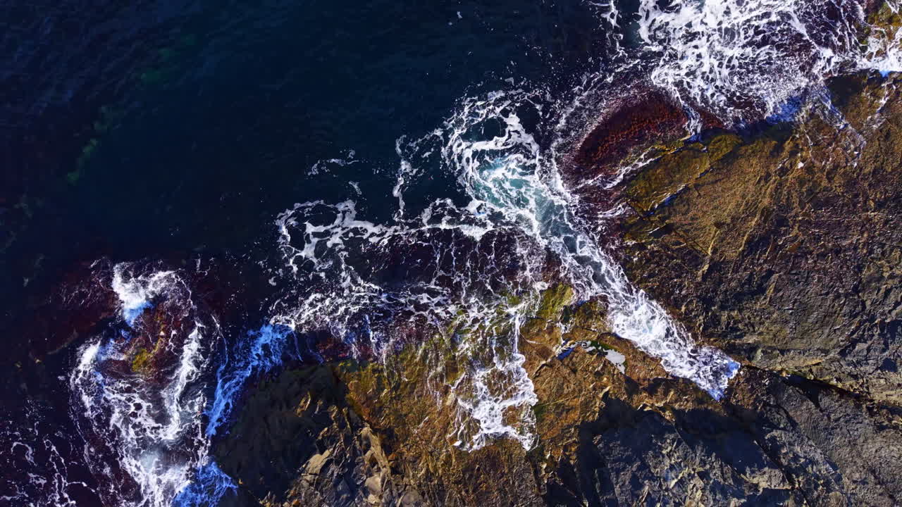 Ocean waves crash against rugged cliffs at sunset, creating a dance of water and light along the coast