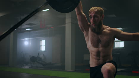 slow motion: man doing single-arm landmine squat-to-press exercise. young man lifting barbell with light weights at gym