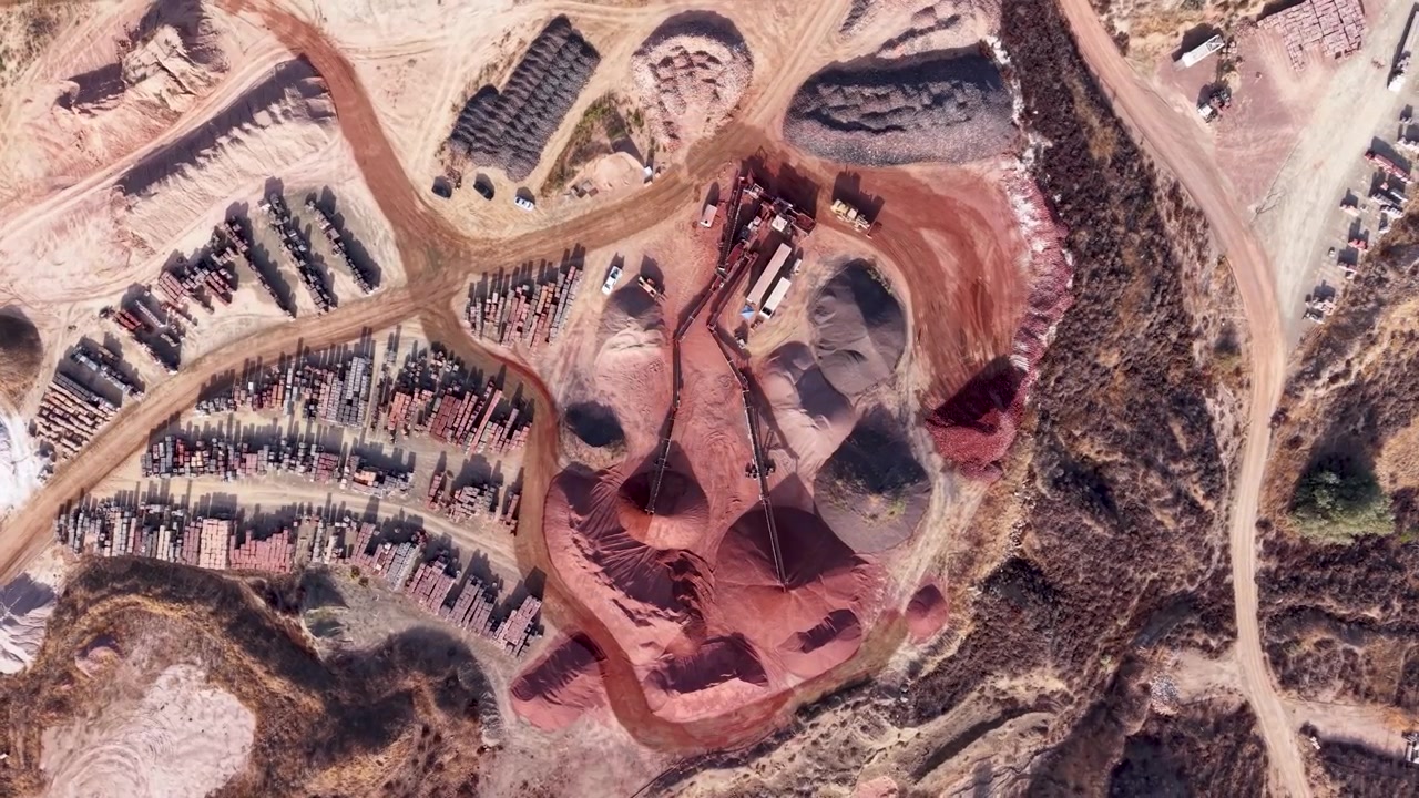 Ziegelverarbeitungsanlage mit Materialhaufen, Maschinen und gestapelten Produkten, Luftaufnahme aus der Vogelperspektive im Orbit mit roten Feldwegen.