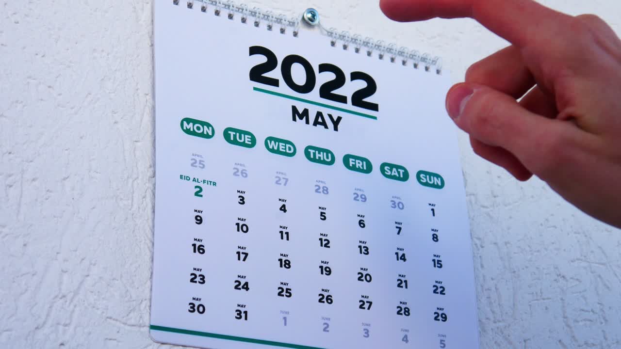 Close-up of male hands tearing off the wall calendar April page 2022 and pointing finger to Eil al-Fitr date on the next one