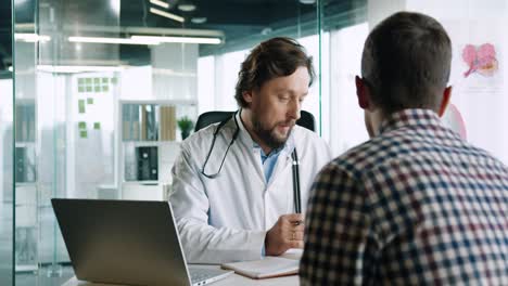 vista de primer plano del médico caucásico sentado en el escritorio con una computadora portátil y explicando al paciente masculino el tratamiento del coronavirus en consulta médica