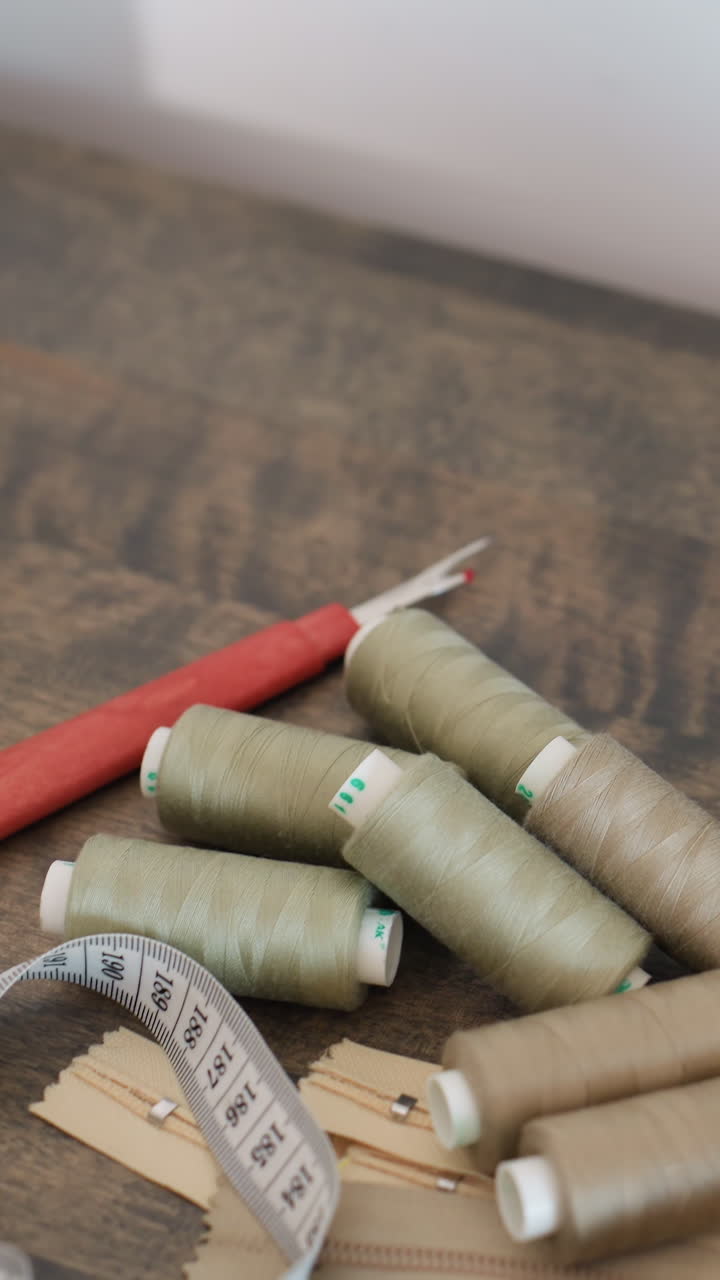 Bobinas de hilo verdes con un quita costuras esparcido sobre un escritorio de madera con cinta métrica y botones, quita costuras listo para deshacer puntadas, sastre rehaciendo el dobladillo, upcycler restaurando la prenda, reparación en el estudio