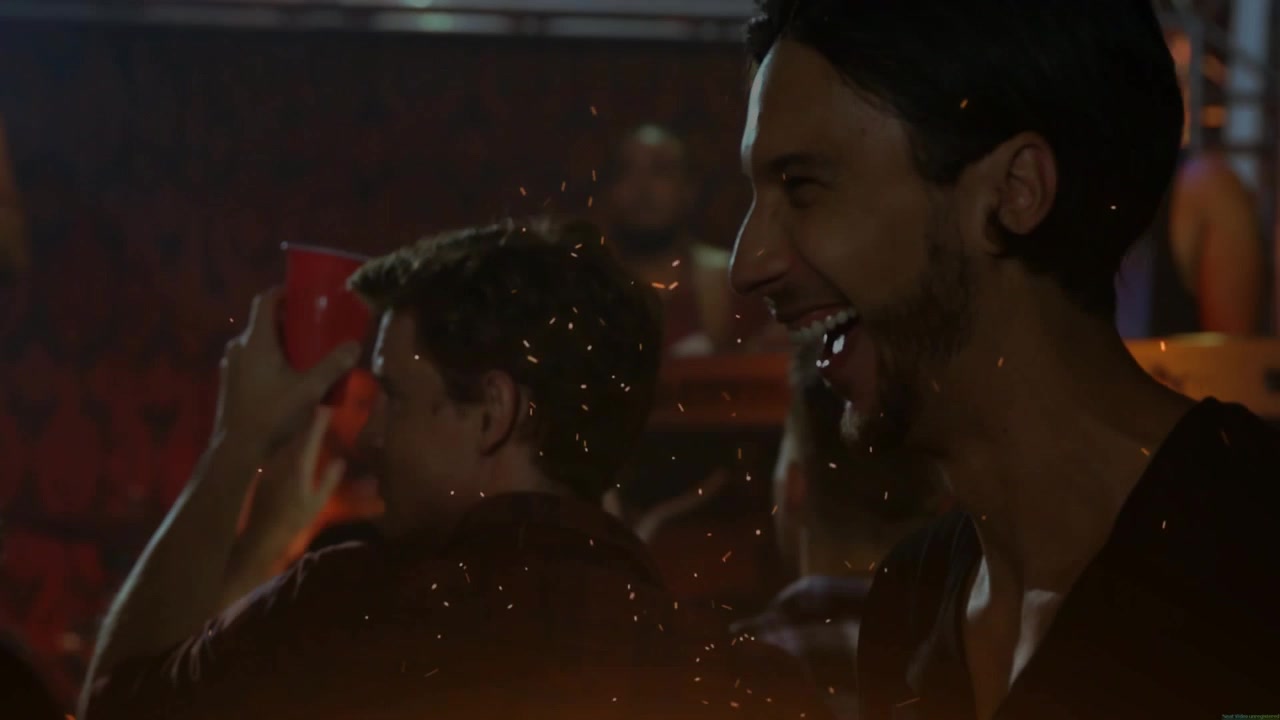 Uomo sorridente che ride, girandosi verso il palco mentre un artista avvia la musica, uomo in secondo piano che alza una tazza rossa
