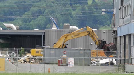 交通と地元の列車が通過するスイスの建物を解体する水力爪付きのコマツ掘削機