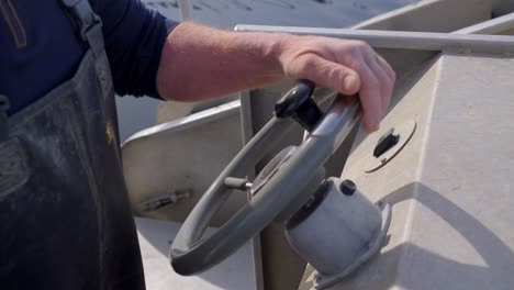 close up of a male sailor stearing the helm of a boat wearing overalls