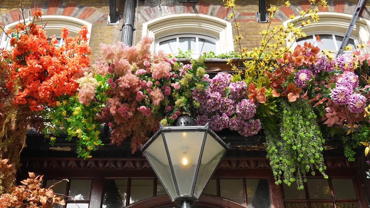 Ingresso di un edificio a Londra decorato con fiori e piante colorati sopra una porta con lampada a sospensione. Vista ravvicinata che mostra la disposizione floreale e i dettagli della facciata.