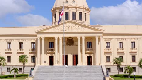 Ascent-shot-with-drone-of-the-Presidential-Palace-of-Dominican-Republic,-overlooking-the-flagpole-of-the-national-flag