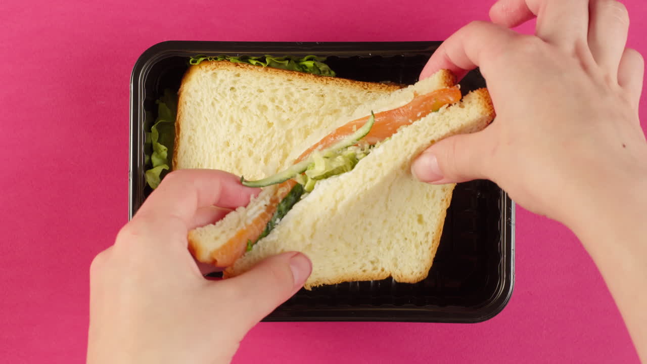Mani che aprono un sandwich al salmone con cetriolo e lattuga