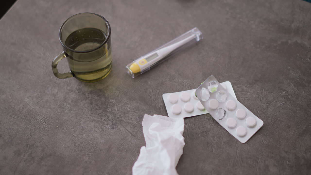 Close-up of medical equipment including used tissue, medication, and glass of water on table, indicating signs of illness recovery with the presence of health-related items