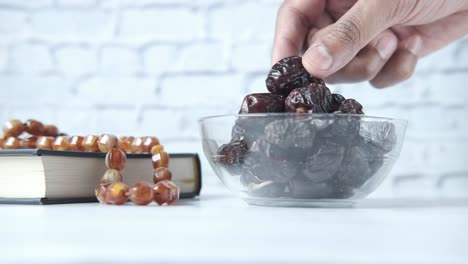 recoger a mano frutas de dátiles frescos en un cuenco y el libro sagrado del corán en la mesa