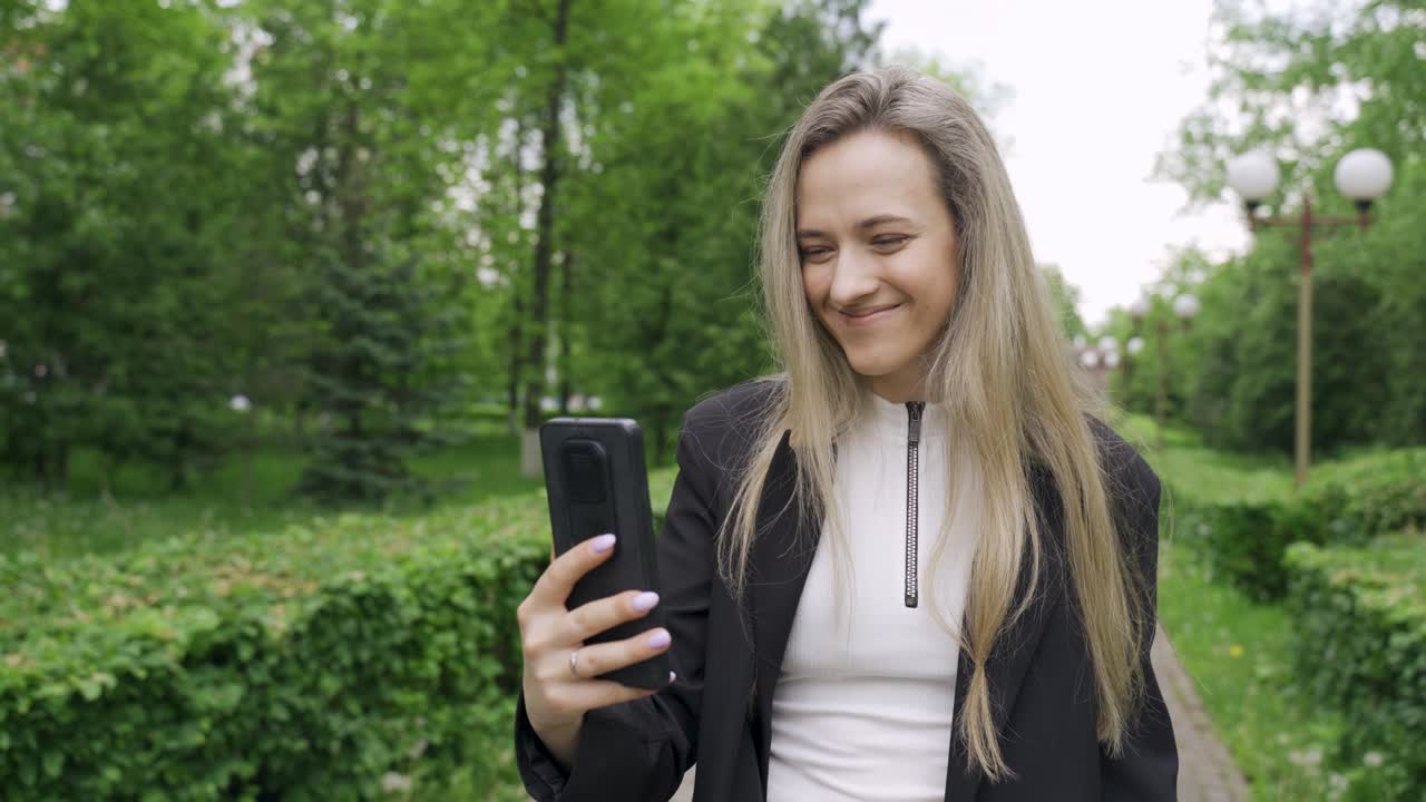 Beautiful young woman takes a selfie on the phone in the park.