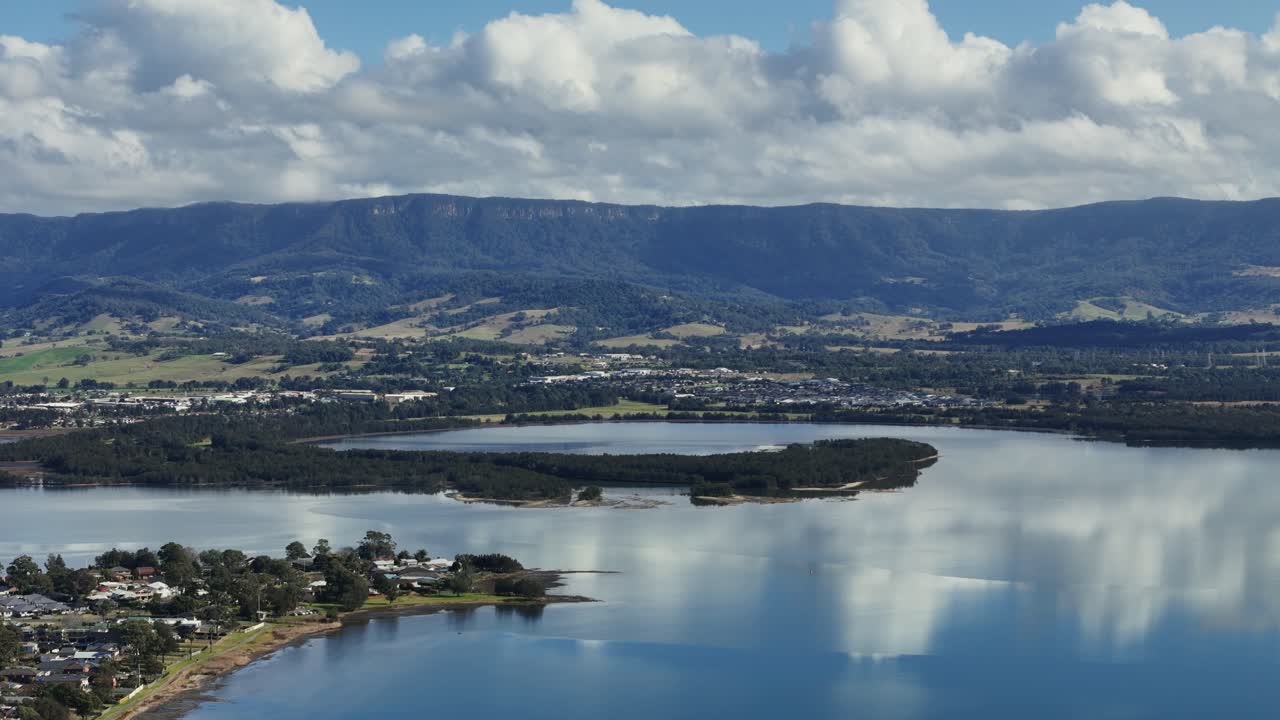 Aerial of Lake Illawarra water reflecting hills and cloudy sky in New South Wales, Australia